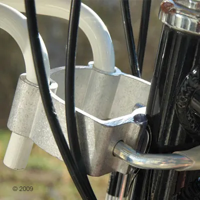 Metalen bevestigingsstuk aan een zwart fietsstuur, met witte en zwarte buizen en kabels zichtbaar. Geen merknaam of tekst aanwezig.