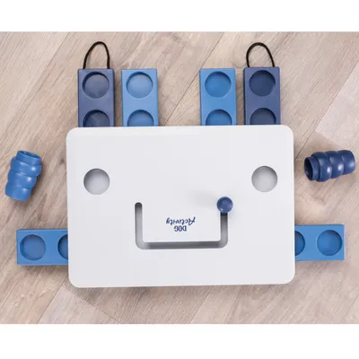 Jeu d’intelligence pour chien, plateau blanc avec inscription « Dog Activity », pièces coulissantes et modules bleus en plastique visibles sur un sol en bois.