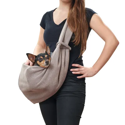 Vrouw draagt een kleine hond in een beige stoffen draagtas over haar schouder. Draagtas voor huisdieren zichtbaar.