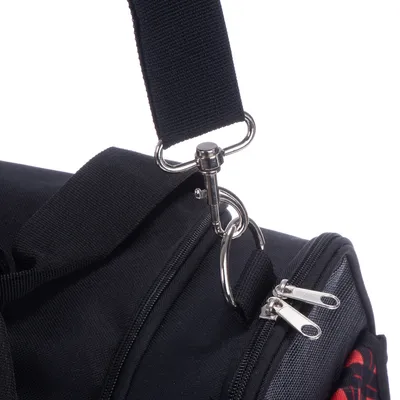Gros plan sur une sangle en tissu noir avec mousqueton métallique fixée à un sac noir, deux fermetures éclair visibles sur le dessus du sac.