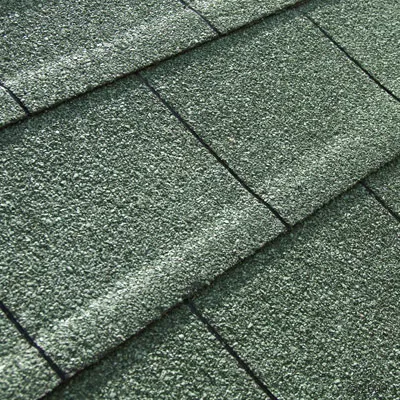 Zbliżenie na zielone dachówki z ziarnistą powierzchnią, ułożone w rzędach. Widoczny materiał przypominający asfalt lub gont bitumiczny.