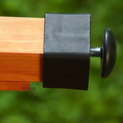 Zbliżenie na drewniany element z czarną plastikową końcówką i metalową śrubą z okrągłą nakrętką, widoczne detale mocowania.