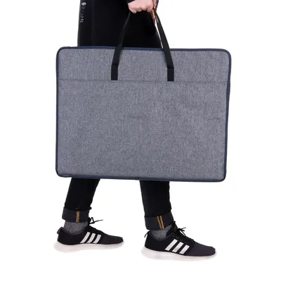Graue Tragetasche mit zwei schwarzen Griffen, von einer Person getragen. Tasche zeigt rechteckige Form und praktische Grösse für Transportzwecke.