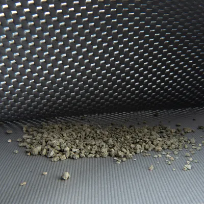 Hoopje kattenbakvullingkorrels op een geribbelde ondergrond met een grijze, gestructureerde achtergrond. Materiaal van de korrels niet zichtbaar.