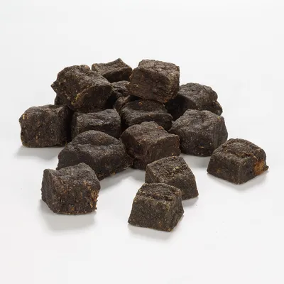 Dunkle, würfelförmige Snacks aus gepresstem Material, sichtbar in einer losen Anordnung auf weissem Hintergrund.