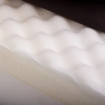 Nahaufnahme von wellenförmigem Schaumstoff und einer schwarzen Stoffschicht, zeigt Materialstruktur für Polsterung oder Matratzen.