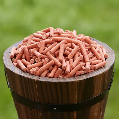 Rote, längliche Futtersticks in einem Holzfass, geeignet für die Darstellung von Tierfutterprodukten.