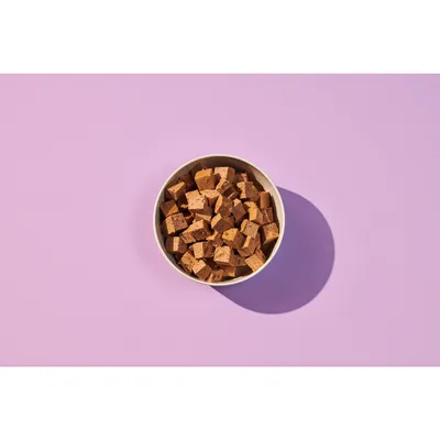 Bowl filled with small brown food cubes, shown from above on a plain background.