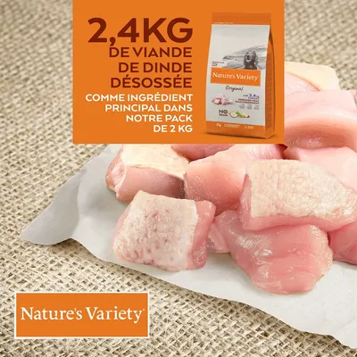 2,4 kg de viande de dinde désossée comme ingrédient principal dans le pack Nature’s Variety Original 2 kg. Morceaux de dinde crue visibles sur papier.