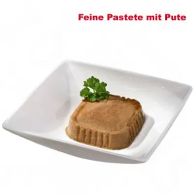 Feine Pastete mit Pute, synlig text på tyska. Kvadratisk portion pastej med persilja på vit tallrik.