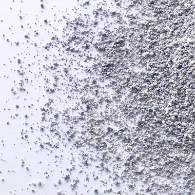 Крупный план серо-белого сыпучего наполнителя для кошачьего туалета на белой поверхности. Видна текстура и размер гранул.