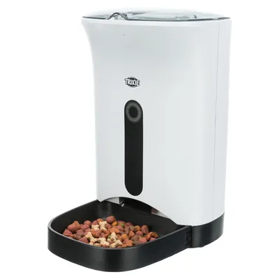 Trixie automatic pet feeder in white with black food tray, filled with dry kibble. Trixie brand name visible on front.
