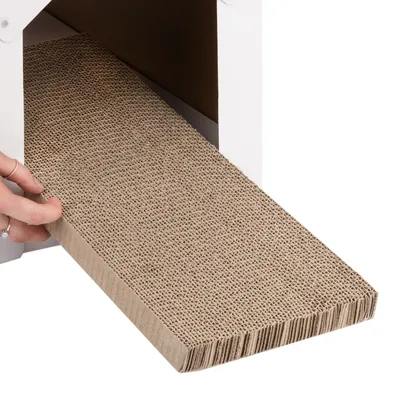 Una mano extrae una alfombrilla rascadora de cartón ondulado intercambiable de una carcasa blanca.