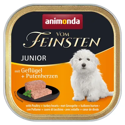 Animonda Vom Feinsten Junior mokré krmivo s drůbežím a krůtími srdci, servírovací návrh s kousky masa na černém talíři, obrázek bílého psa.