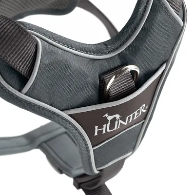 Szelki dla psa z szarego materiału z odblaskowymi szwami, metalowym kółkiem i logo Hunter na czarnej skórzanej etykiecie.