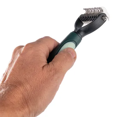 Hand houdt een ontklittingskam met ergonomisch handvat en metalen tanden voor vachtverzorging.