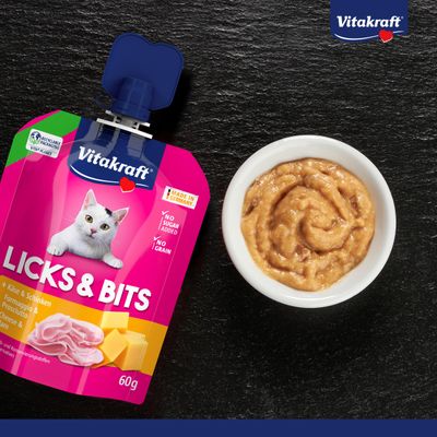 Vitakraft Licks & Bits Cheese & Ham, Made in Germany, no sugar, no grains, recyclable packaging, 60g. Product next to bowl with food.