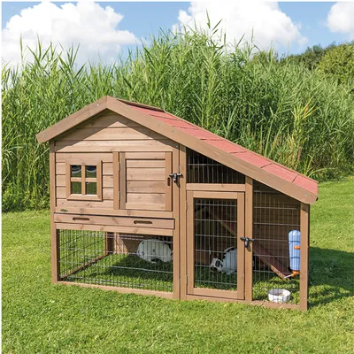 Wooden outdoor hutch with red roof, mesh wire panels, two doors, water bottle and bowl visible. Two white rabbits inside on grass. Hutch has small window and ramp between levels.