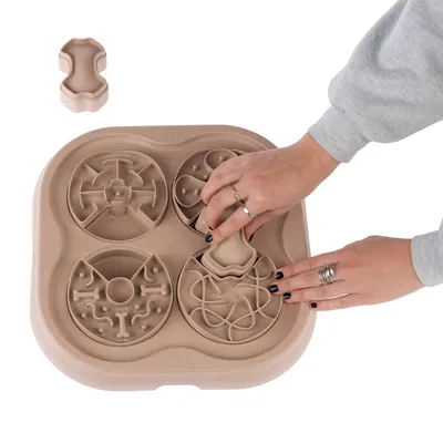 Plateau interactif beige à quatre compartiments avec motifs différents, main ajustant une pièce centrale en forme d’os. Matériau visible : plastique.