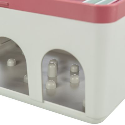 Detailweergave van een wit speelgoed met roze bovenkant en meerdere kleine pinnetjes binnenin, zichtbaar door boogvormige openingen.