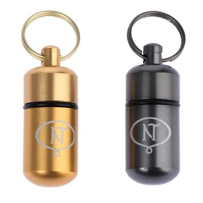 Två metallbrickor i guld och svart med graverad 'NT'-logotyp, vardera med nyckelring.