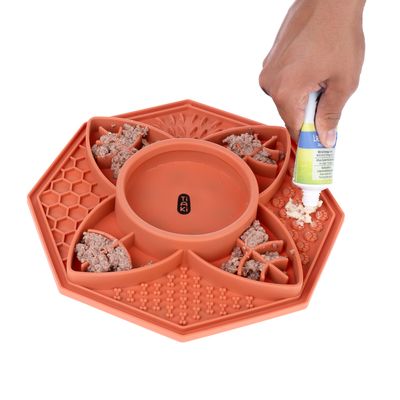 Tiaki Futtermatte aus Silikon mit verschiedenen Texturen, befüllt mit Nassfutter und Paste. Hand trägt Paste auf die Matte auf.