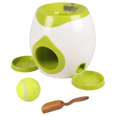 Distributeur blanc et vert avec ouverture frontale, deux plateaux verts, une balle de tennis jaune et une pelle marron visibles devant l’appareil. Aucun texte ou marque visible.