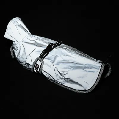 Zilverkleurige hondenjas met reflecterend materiaal, verstelbare riemen en zwarte sluiting. Geschikt voor koude of donkere omgevingen.