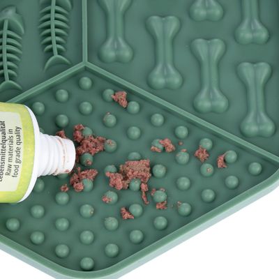 Grüne Silikonmatte mit Knochen- und Fischmuster, darauf verstreut Nassfutter aus einer Tube. Geeignet für langsames Fressen oder Beschäftigung.