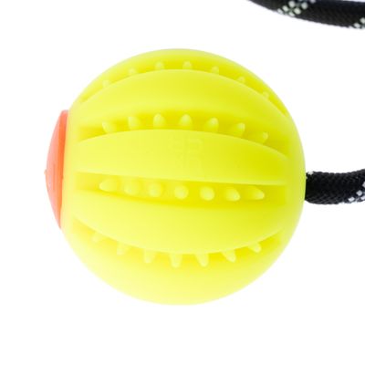 Balle jaune en caoutchouc avec picots et rainures, corde noire attachée, partie latérale orange visible. Aucun texte de marque lisible.