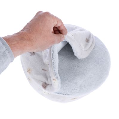 Main soulevant l’ouverture d’un couchage rond en tissu doux gris clair à motifs, montrant l’intérieur du produit.