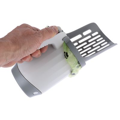 Hand houdt grijze schep met geïntegreerde container en bevestigde groene zak met pootafdrukken, geschikt voor het reinigen van dierenstrooisel.