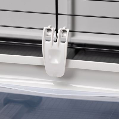 Fermeture en plastique blanc sur cage à barreaux métalliques noirs, fixation visible entre la base et la grille supérieure.