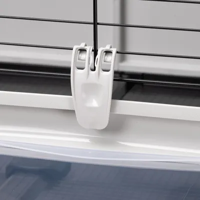 Fermeture en plastique blanc sur cage à barreaux métalliques noirs, fixation visible entre la base et la grille supérieure.