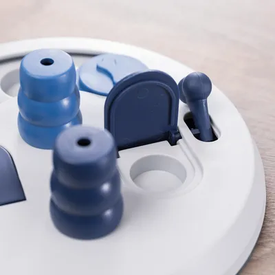 Кръгла бяла играчка със сини елементи, включително вратички, лостчета и части за подреждане. Подпомага интерактивна игра.