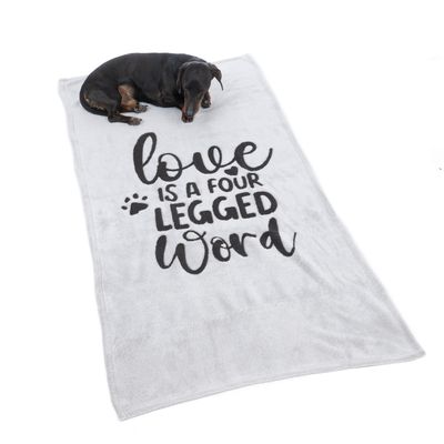 Coperta grigia con scritta nera 'Love is a four legged word' e impronta di zampa. Cane sdraiato sulla coperta.