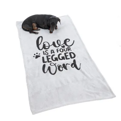 Coperta grigia con scritta nera 'Love is a four legged word' e impronta di zampa. Cane sdraiato sulla coperta.