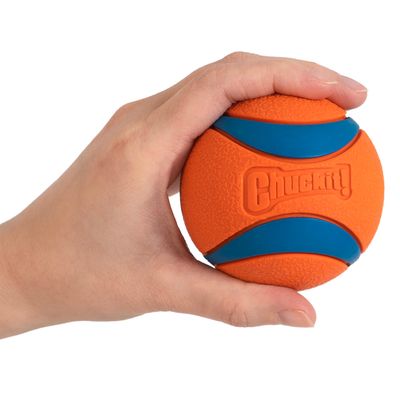 Chuckit! pelota naranja y azul sostenida en la mano, muestra el tamaño y la textura del juguete.