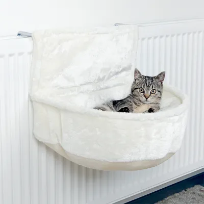 Katzenliege aus weissem Plüsch, befestigt an einem Heizkörper. Graue Katze liegt entspannt in der Liege.