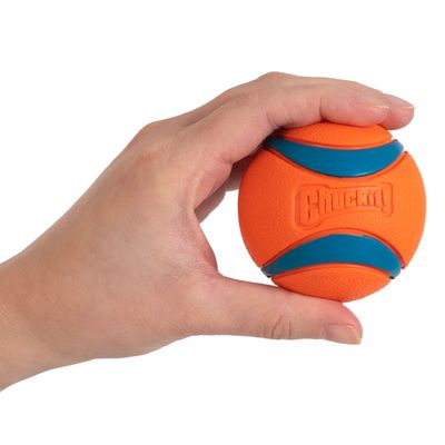 Chuckit! pelota naranja con rayas azules, sostenida en una mano. Muestra el tamaño y el diseño de la pelota.