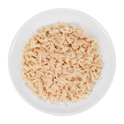 Primo piano di carne di pollo cotta e sminuzzata su un piatto bianco.