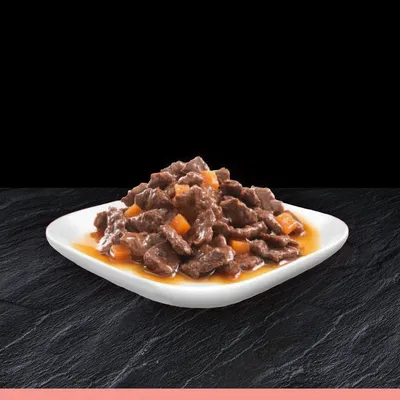 Portie natvoer met stukjes vlees en oranje groenten in saus, geserveerd op een wit bord.