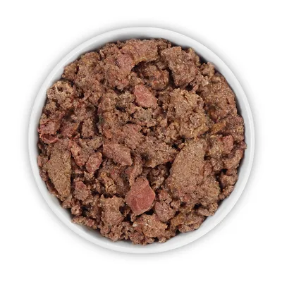 Primer plano de comida húmeda en un cuenco blanco, compuesta por trozos de carne marrones y rojos.