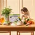 Dog sitting at table with Forthglade senior complete meal box, surrounded by fresh ingredients including carrots, peas, herbs and oils, showing product and its natural components.