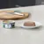 Boîte de pâtée Ziwi Peak NZ Lamb Recipe 92 % viande visible, à côté d'une portion servie sur une assiette blanche. Texte anglais sur l'emballage.