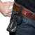 Black bag dispenser with belt clip, attached to a belt. Black waste bags are pulled from the opening.