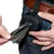 Black pouch dispenser with zip, attached to a belt. A hand pulls out a black dog waste bag.