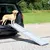 Hond staat op een uitgeschoven, lichtgrijze hondenloopplank van metaal die vanuit de kofferbak van een auto naar de grond loopt. Product toont gebruik van de loopplank.
