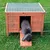 Wooden small animal house with green roof and ramp, surrounded by metal fence. Grey rabbit leaves the house via the ramp.