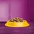 Bowl filled with assorted dry pet food pieces in various shapes and colours, displayed on a purple surface.